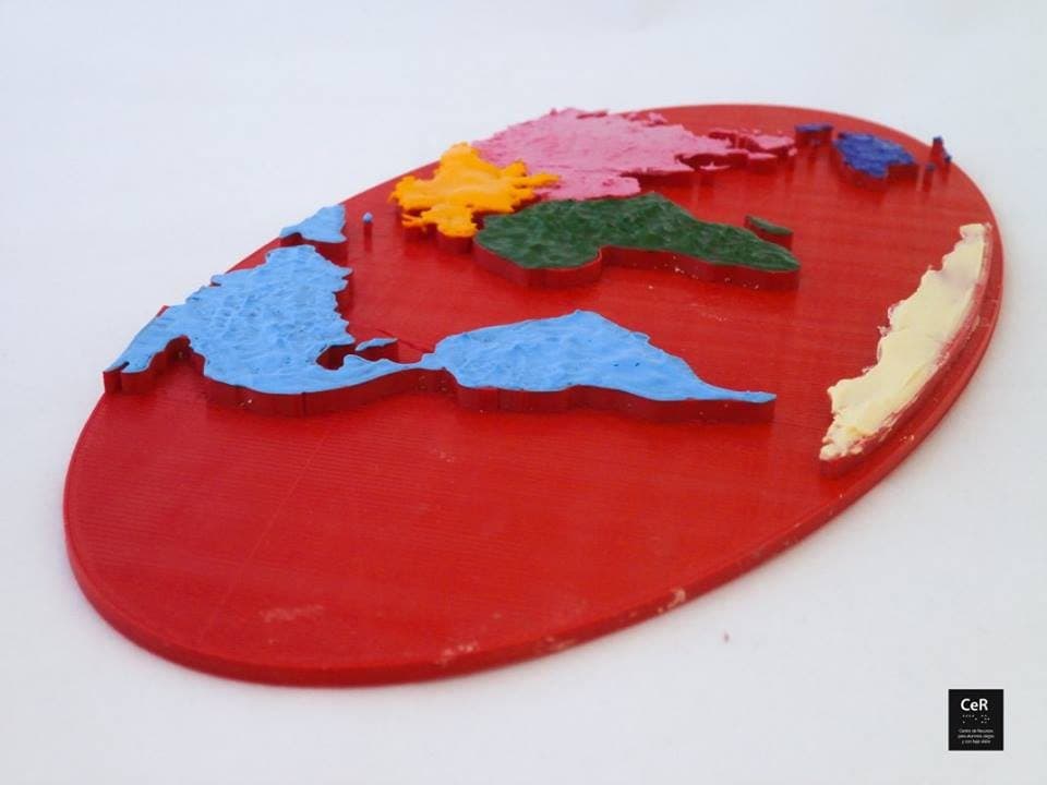 Planisferio impreso en 3D sobre base roja ovalada, con los continentes en relieve y en distintos colores.