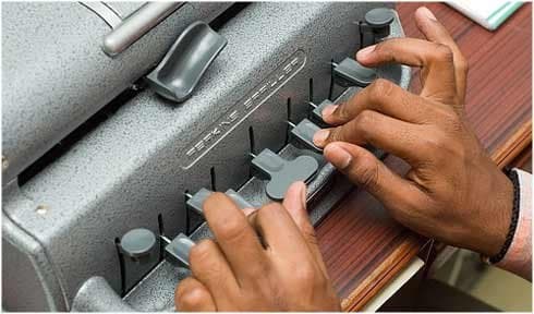 Manos escribiendo sobre las teclas de una máquina de escribir braille Perkins.