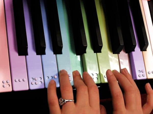 Dos manos tocando un piano cuyas teclas están rotuladas con puntos braille en relieve.