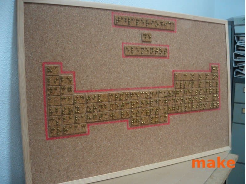Tabla periódica de los elementos construida en relieve sobre un tablero de corcho, con cada elemento escrito en braille.